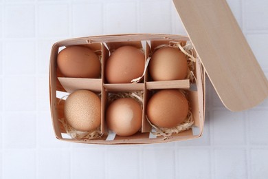 Photo of Raw chicken eggs in wooden egg tray on white tiled table, top view