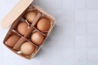 Photo of Raw chicken eggs in wooden egg tray on white tiled table, top view. Space for text