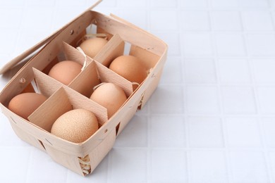Photo of Raw chicken eggs in wooden egg tray on white tiled table, closeup. Space for text