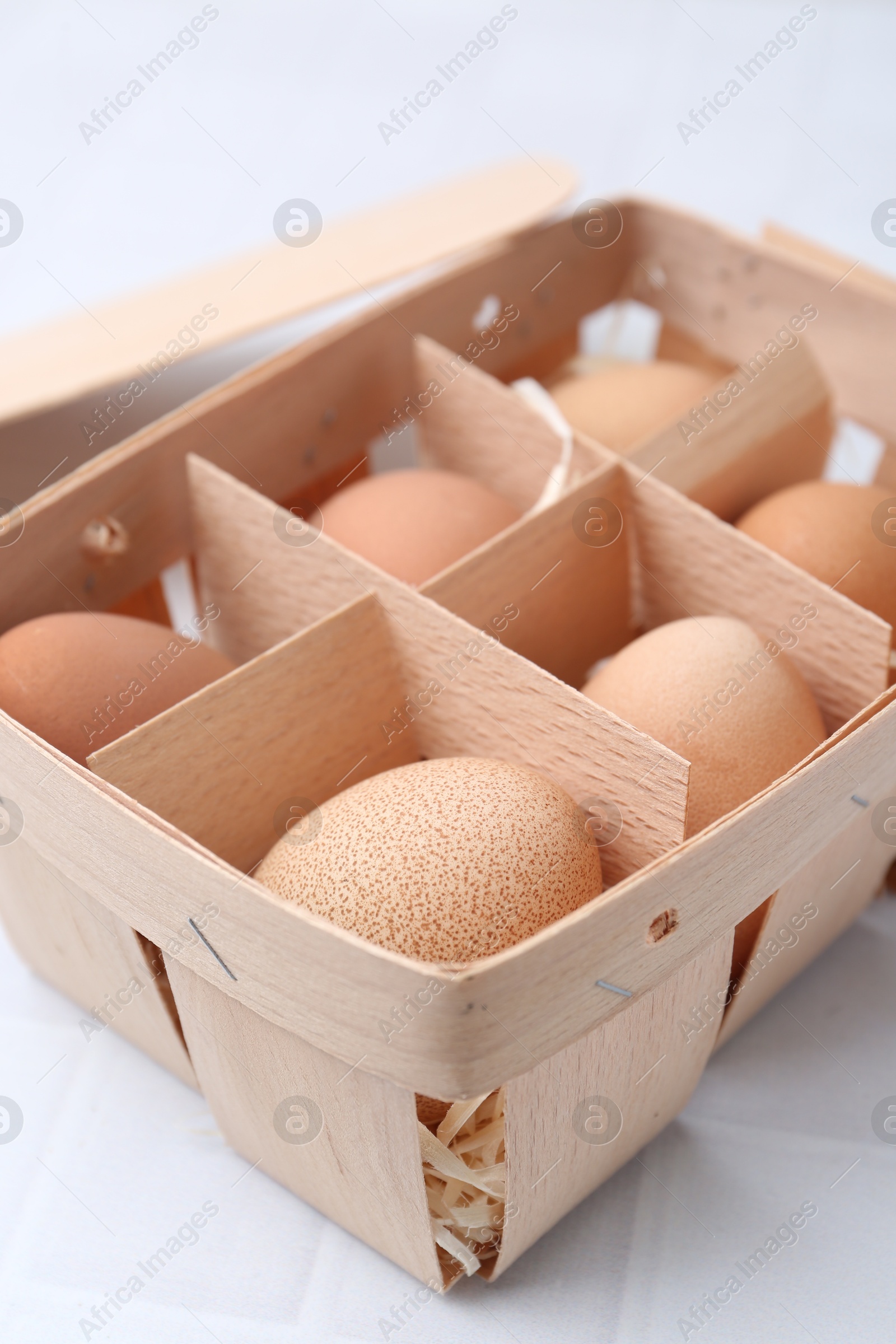 Photo of Raw chicken eggs in wooden egg tray on white tiled table, closeup