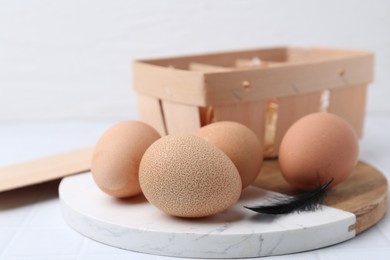 Photo of Raw chicken eggs and wooden egg tray on white tiled table, closeup