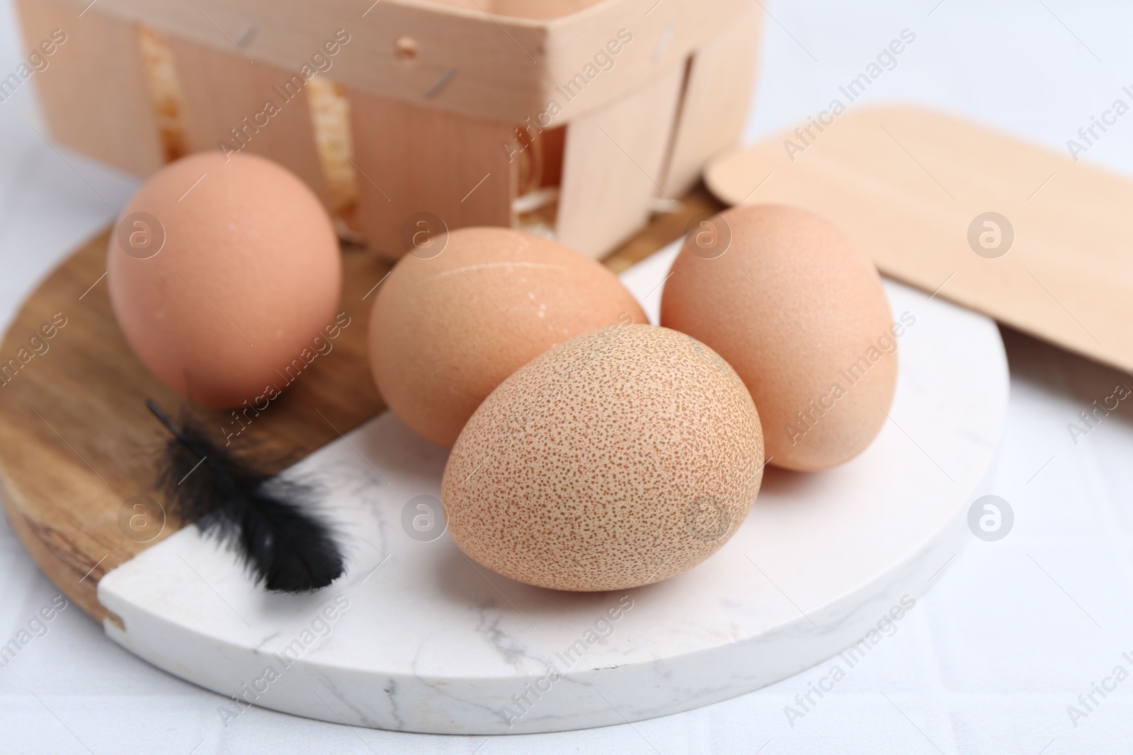 Photo of Raw chicken eggs and wooden egg tray on white tiled table, closeup