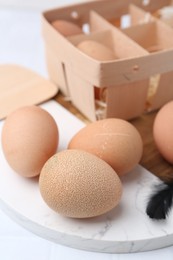 Photo of Raw chicken eggs and wooden egg tray on white tiled table, closeup