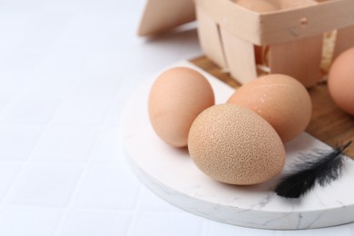 Photo of Raw chicken eggs and wooden egg tray on white tiled table, closeup. Space for text