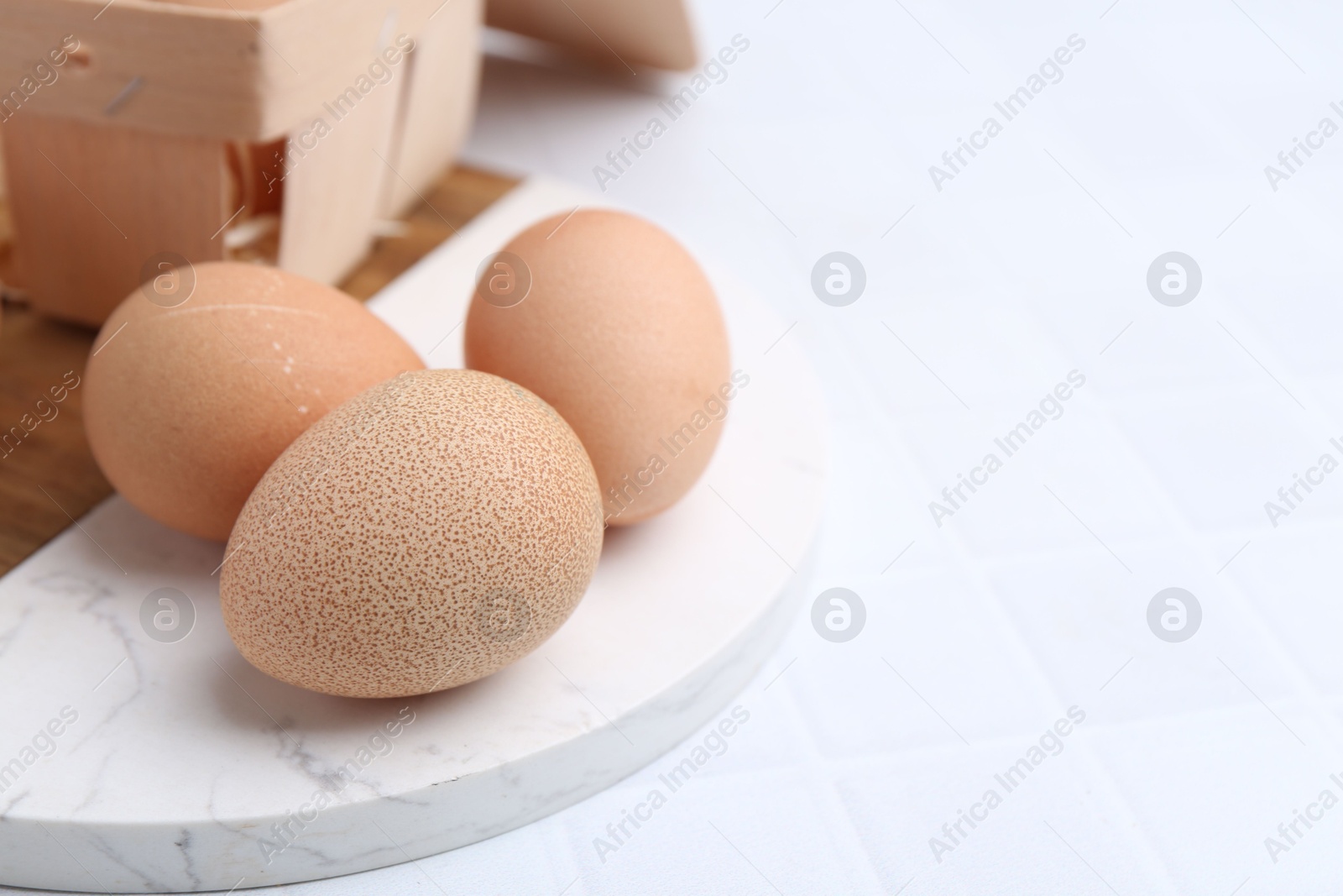 Photo of Raw chicken eggs and wooden egg tray on white tiled table, closeup. Space for text