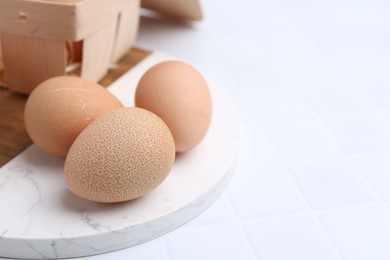 Photo of Raw chicken eggs and wooden egg tray on white tiled table, closeup. Space for text