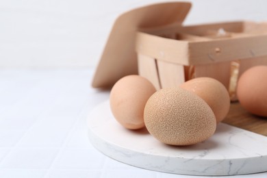 Photo of Raw chicken eggs and wooden egg tray on white tiled table, closeup. Space for text