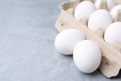 Photo of Raw chicken eggs in egg carton on grey table, closeup. Space for text