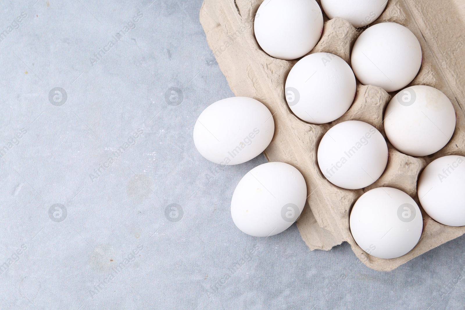 Photo of Raw chicken eggs in egg carton on grey table, top view. Space for text