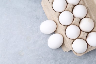 Photo of Raw chicken eggs in egg carton on grey table, top view. Space for text