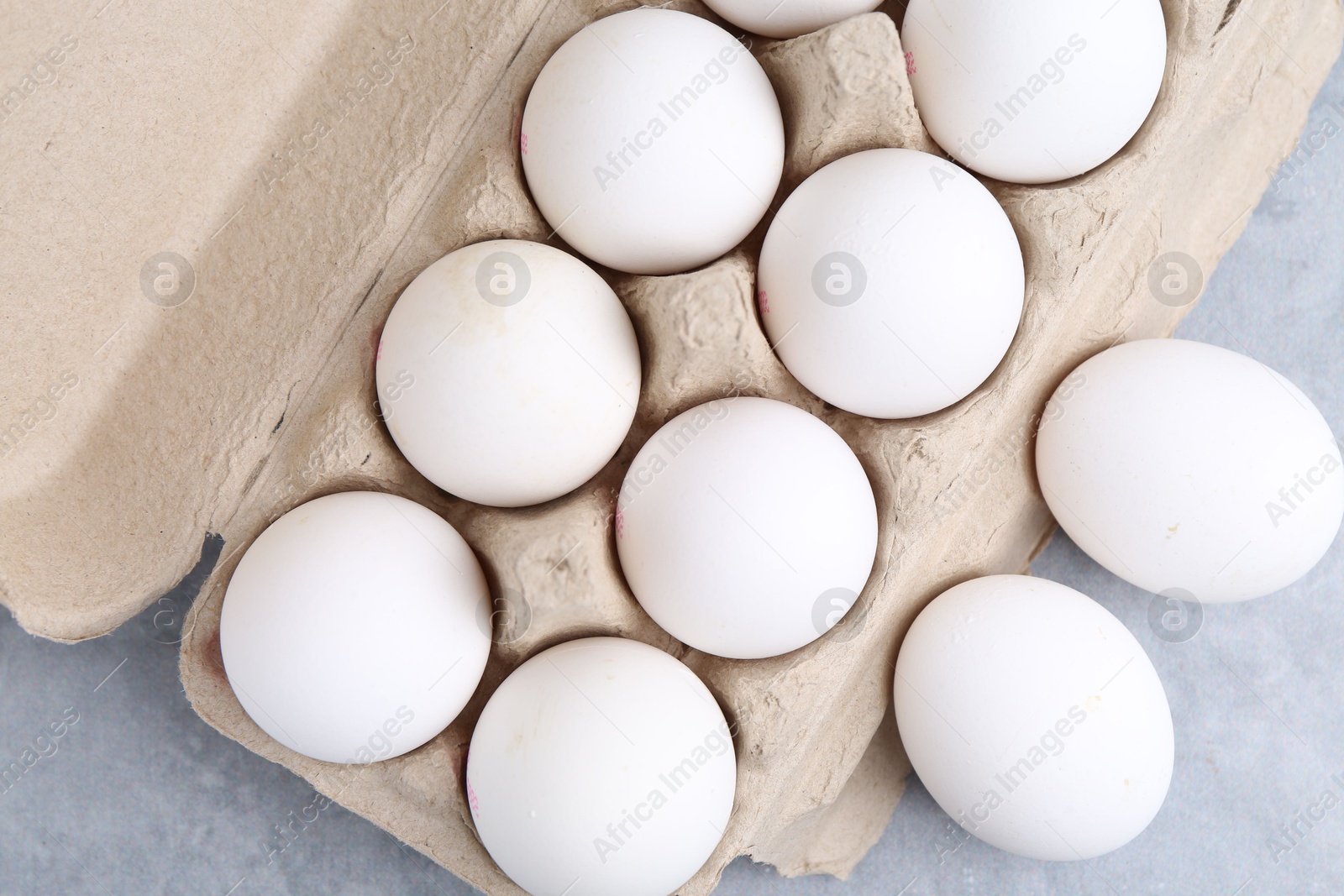 Photo of Raw chicken eggs in egg carton on grey table, top view