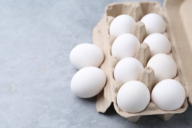 Photo of Raw chicken eggs in egg carton on grey table, closeup. Space for text