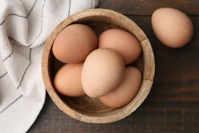 Photo of Raw chicken eggs in bowl on wooden table, top view