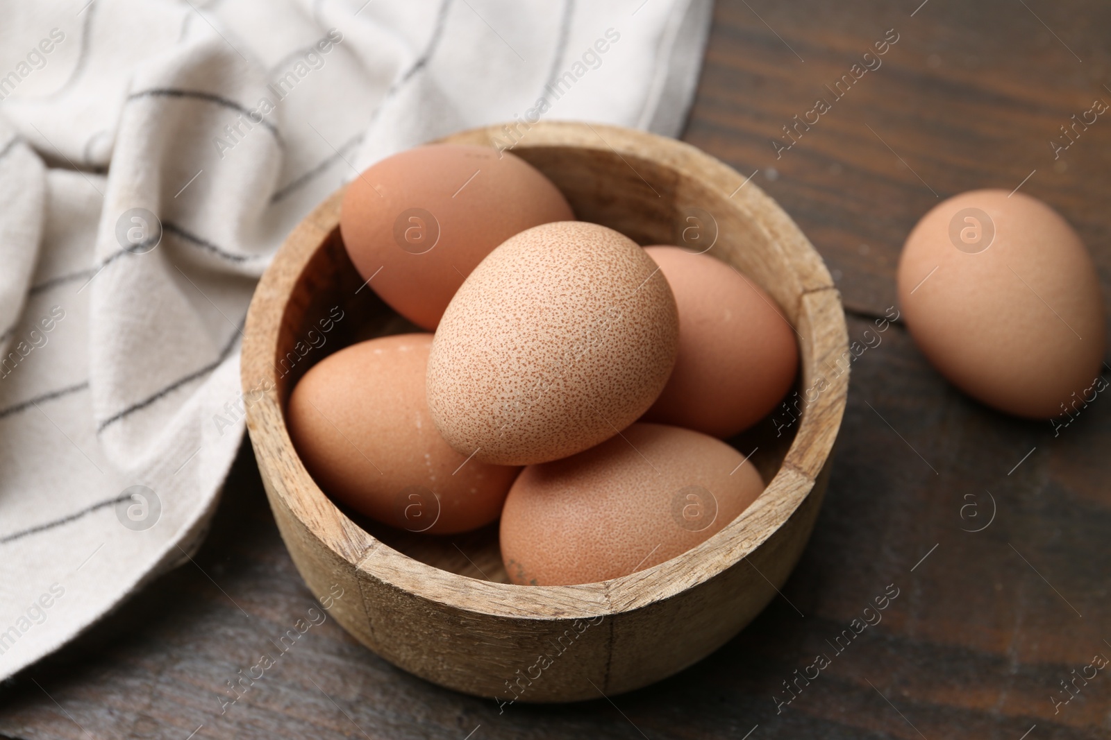 Photo of Raw chicken eggs in bowl on wooden table, closeup