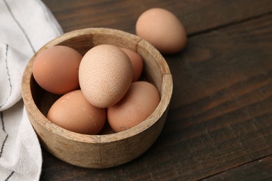 Photo of Raw chicken eggs in bowl on wooden table, closeup. Space for text