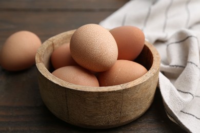 Photo of Raw chicken eggs in bowl on wooden table, closeup
