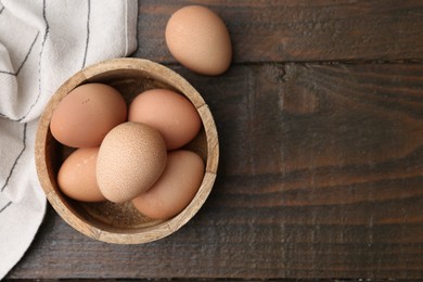 Photo of Raw chicken eggs in bowl on wooden table, top view. Space for text