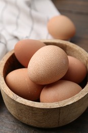 Photo of Raw chicken eggs in bowl on wooden table, closeup
