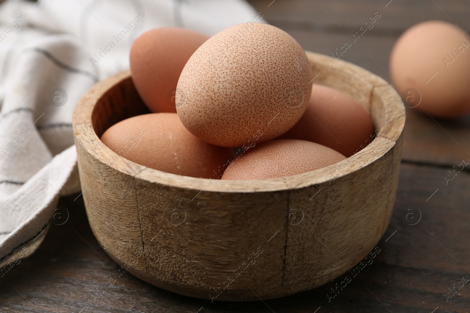 Photo of Raw chicken eggs in bowl on wooden table, closeup