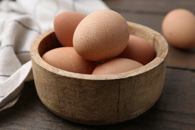 Photo of Raw chicken eggs in bowl on wooden table, closeup