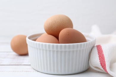 Photo of Raw chicken eggs in bowl on white wooden table, closeup