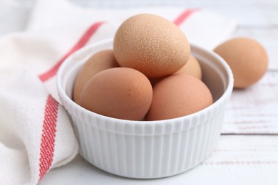Photo of Raw chicken eggs in bowl on white wooden table, closeup