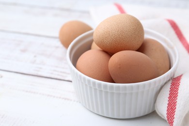 Photo of Raw chicken eggs in bowl on white wooden table, closeup. Space for text