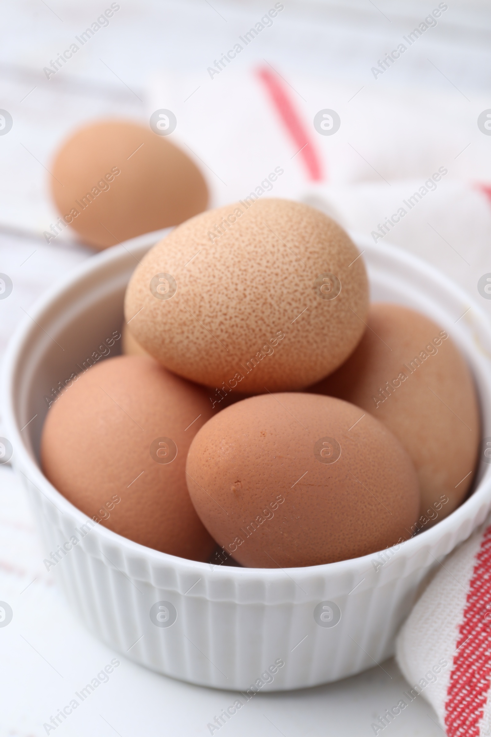 Photo of Raw chicken eggs in bowl on white wooden table, closeup