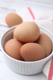 Photo of Raw chicken eggs in bowl on white wooden table, closeup
