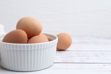 Photo of Raw chicken eggs in bowl on white wooden table, closeup. Space for text