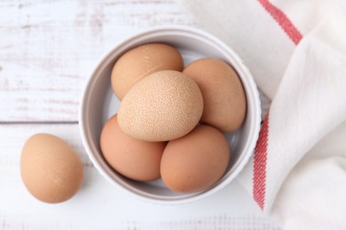 Photo of Raw chicken eggs in bowl on white wooden table, top view
