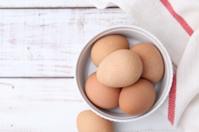 Photo of Raw chicken eggs in bowl on white wooden table, top view. Space for text