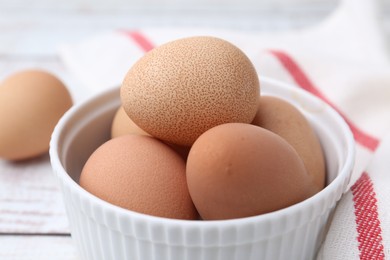 Photo of Raw chicken eggs in bowl on white wooden table, closeup