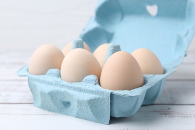 Photo of Raw chicken eggs in egg carton on white wooden table, closeup