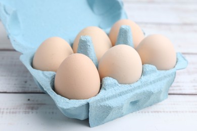 Photo of Raw chicken eggs in egg carton on white wooden table, closeup