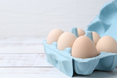 Photo of Raw chicken eggs in egg carton on white wooden table, closeup. Space for text