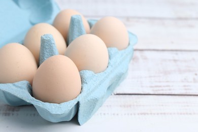 Photo of Raw chicken eggs in egg carton on white wooden table, closeup. Space for text