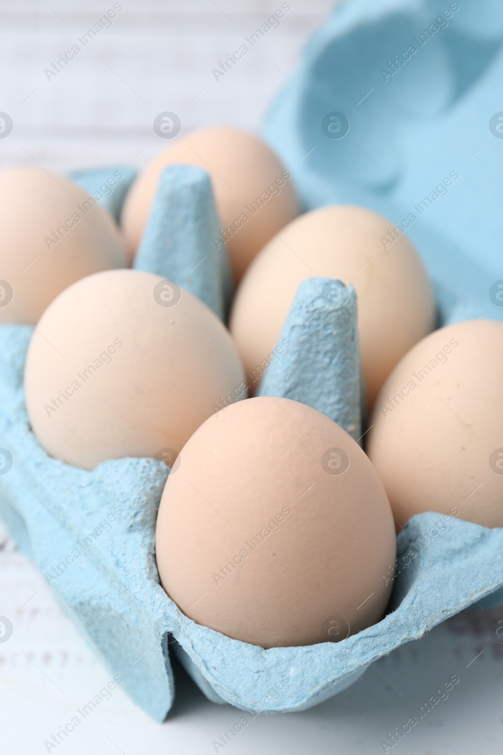 Photo of Raw chicken eggs in egg carton on white wooden table, closeup