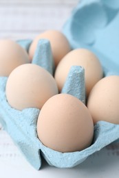 Photo of Raw chicken eggs in egg carton on white wooden table, closeup