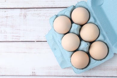 Photo of Raw chicken eggs in egg carton on white wooden table, top view. Space for text