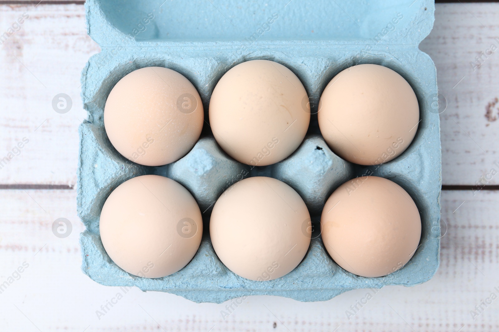 Photo of Raw chicken eggs in egg carton on white wooden table, top view