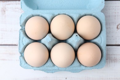 Photo of Raw chicken eggs in egg carton on white wooden table, top view