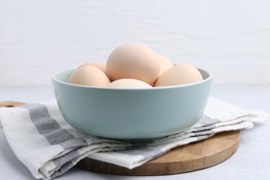 Photo of Raw chicken eggs in bowl on white table, closeup