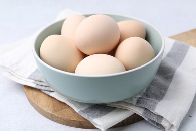 Photo of Raw chicken eggs in bowl on white table, closeup