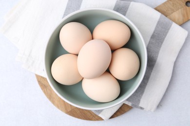 Photo of Raw chicken eggs in bowl on white table, top view