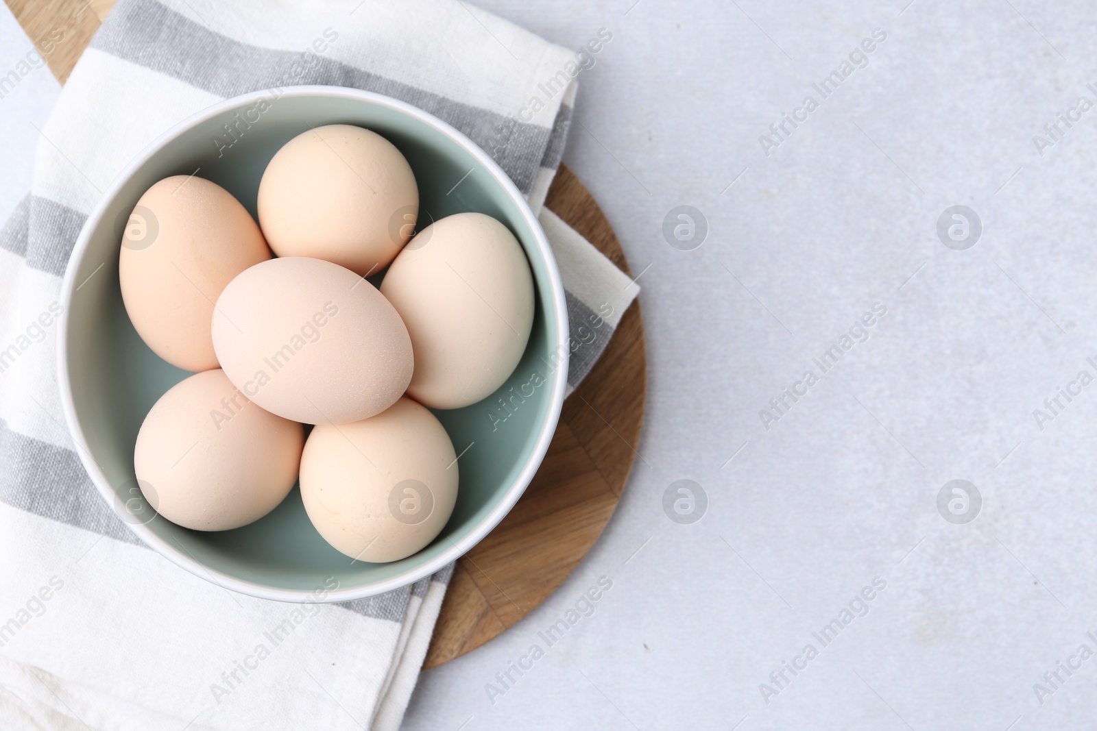 Photo of Raw chicken eggs in bowl on white table, top view. Space for text