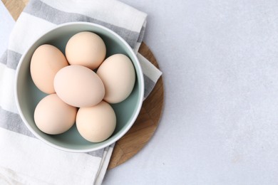 Photo of Raw chicken eggs in bowl on white table, top view. Space for text