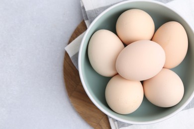 Photo of Raw chicken eggs in bowl on white table, top view. Space for text
