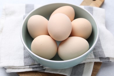 Photo of Raw chicken eggs in bowl on white table, closeup