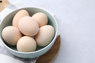 Photo of Raw chicken eggs in bowl on white table, closeup. Space for text